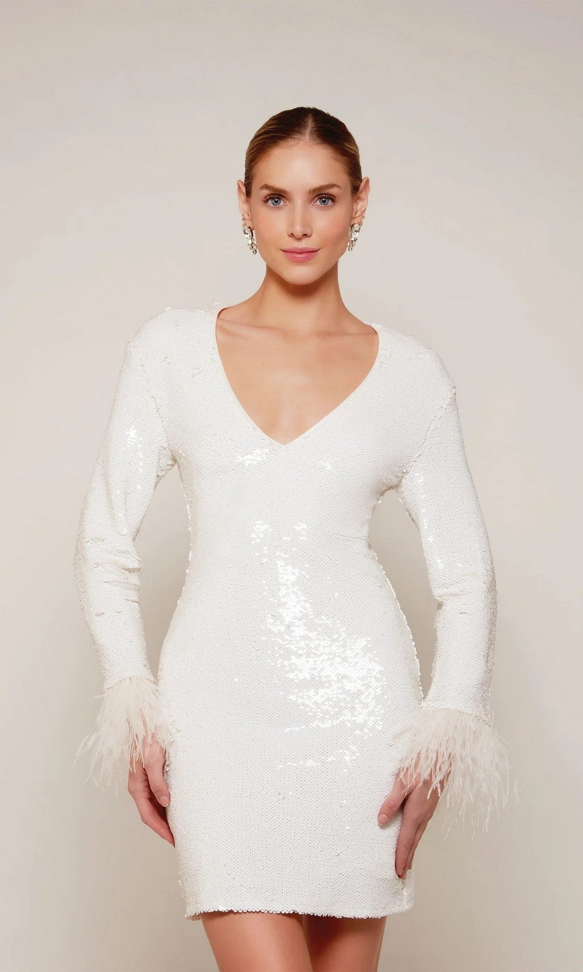 A woman in the Alyce 70027 knee-length white party dress, featuring long sleeves, sequins, a V-neckline, and feather-trim cuffs, stands against a plain background.